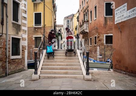 VENISE, ITALIE - AVRIL 2020: Les personnes avec des masques de protection traversent un pont dans le ghetto juif de Venise pendant le verrouillage national de Covid-19 pande Banque D'Images