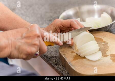 Femme senior coupe l'oignon sur une planche en bois dans la cuisine. Banque D'Images