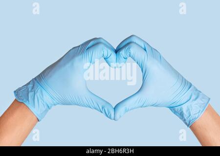 Les mains du médecin dans des gants de protection qui forment le cœur sur fond bleu. Banque D'Images