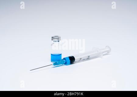 Seringue avec vaccin dans un flacon flacon contenant du liquide bleu sur fond blanc. Concept de médecine et de santé face à une pandémie ou à un virus. Banque D'Images