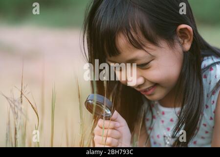 Une jeune fille asiatique heureuse explorant la nature avec une loupe Banque D'Images