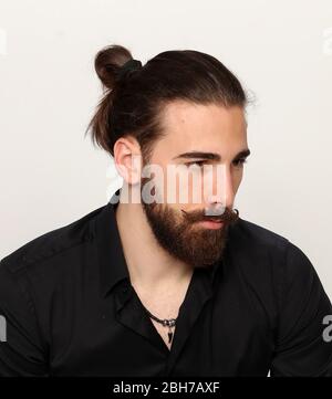 Jeune, modèle masculin tendance avec cheveux longs et barbe posé en studio sur un arrière-plan isolé. Mode, affaires, concept de modélisation. Banque D'Images