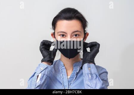 La fille en gants met sur un masque médical. Prévention des maladies virales du rhume et de la grippe. Fond gris clair. Dans un masque respiratoire. Banque D'Images