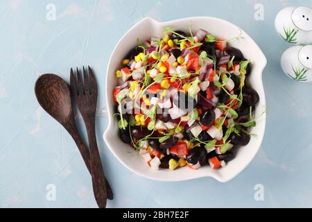 Salade de haricots noirs, maïs, bâtonnets de crabe et microcéréales de pois dans un bol blanc sur fond bleu clair, vue du dessus Banque D'Images