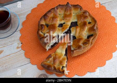 la cuisine maison, une tarte, une tranche de tarte aux pommes remplie de cerises et de noix et une tasse de thé sont sur la table Banque D'Images