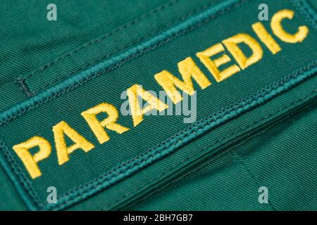 Vue rapprochée et coudée d'un badge britannique PARAMÉDIC cousue sur un maillot paramédic vert. Banque D'Images
