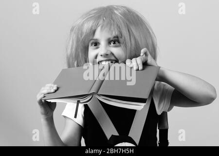 Élève en uniforme scolaire avec perruque rose. Fille morde grand livre bleu. Retour au concept d'école et d'éducation. Fille de l'école avec vue heureuse isolée sur fond rose. Banque D'Images