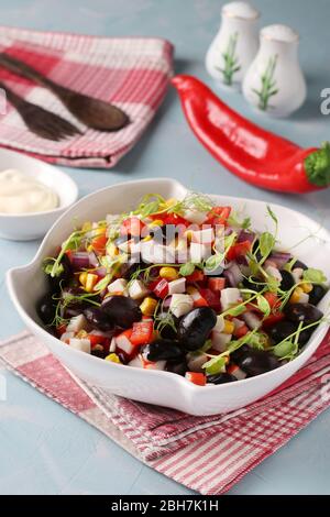 Salade de haricots noirs, maïs, bâtonnets de crabe et microcéréales de pois dans un bol blanc sur fond bleu clair, gros plan Banque D'Images