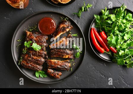 Côtes levées grillées chaud épicé sur plaque sur fond noir en noir. La viande barbecue savoureux. Haut de la vue, télévision lay Banque D'Images