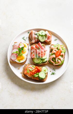 Sandwichs à surface ouverte avec viande, légumes, fruits de mer sur plaque sur fond de pierre claire avec espace texte libre. En-cas savoureux et sains. Banque D'Images