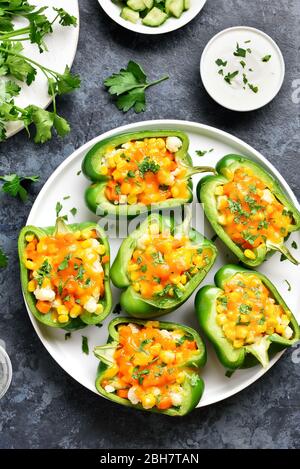 Poivrons verts farcis avec du maïs, carotte, chou-fleur sur plaque blanche sur fond noir en bleu. Saine alimentation Une alimentation végétarienne ou concept. Vue d'en haut Banque D'Images