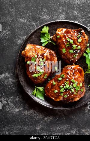 Gros plan sur fond de pierre noire des cuisses de poulet grillé au miel sucré et épicé. Cuisine savoureuse dans un style asiatique. Vue sur le dessus, plat Banque D'Images