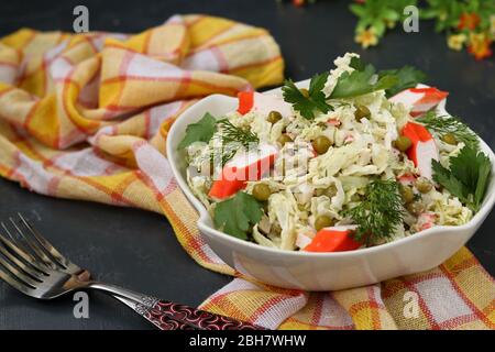 Salade saine avec chou chinois, pois en conserve et bâtonnets de crabe dans un bol sur fond sombre Banque D'Images