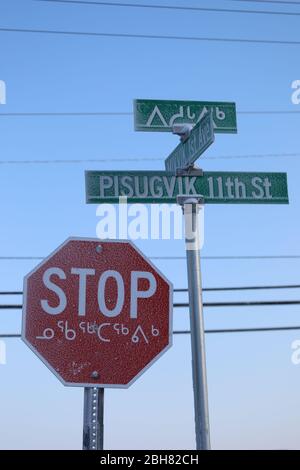 Panneau rouge double langue avec panneaux de signalisation multilingues en arrière-plan, dans la communauté d'Arviat, au Nunavut. Le panneau stop et les panneaux de rue Banque D'Images