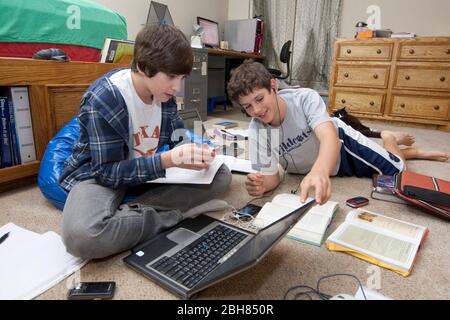 Austin Texas Etats-Unis, 23 octobre 2009: Garçons de septième année, 13 ans, faisant des devoirs en utilisant des manuels traditionnels avec des ordinateurs portables, des écouteurs et des téléphones cellulaires utilisés pour envoyer des textes à d'autres étudiants dans leur groupe d'étude. Modèles OK © Bob Daemmrich © Bob Daemmrich Banque D'Images