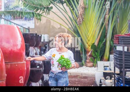 Femme aux cheveux bouclés blonds ressemble à une vase avec un plant de basilic à la main. Boutique jardin concept et des personnes Banque D'Images