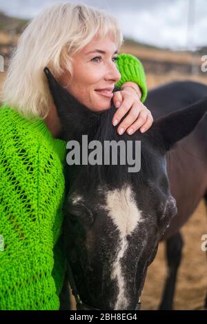 Concept d'amour pour les gens et animlas ensemble dans le bonheur et l'amitié. Beaitufl blonde femme et cheval sombre dans un endroit pittoresque en plein air embrassant et aimant Banque D'Images