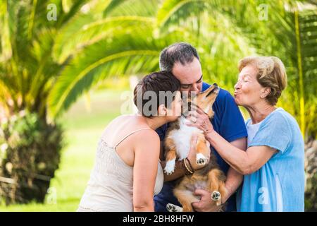 Famille de thérapie alternative les générations d'âge différentes se câlin et s'amuser avec un chien de chiot animal de compagnie au milieu - vert naturel avec les arbres et les personnes heureux avec le concept animal Banque D'Images