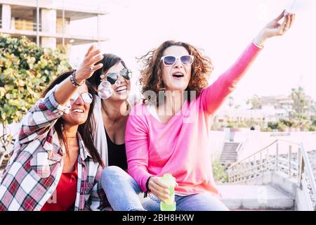 Trois jeunes femmes qui s'amusent en plein air à jouer avec du savon moussant - scène plein de bonheur et de bonheur avec des gens joyeux qui profitent ensemble la journée - image vive avec fond blanc Banque D'Images