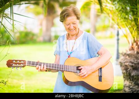 Une femme caucasienne âgée de bonne humeur et heureuse souriante et jouant de la guitare et de la musique de dong dans les activités de loisirs en plein air du parc - des personnes heureuses à la retraite avec des intérêts appréciant la nouvelle vie Banque D'Images