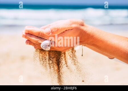 Environnement et respect de la nature avec près des mains de femmes prenant le sable tombant vers le bas - plage et ciel bleu océan en arrière-plan - vacances d'été concept de vacances Banque D'Images