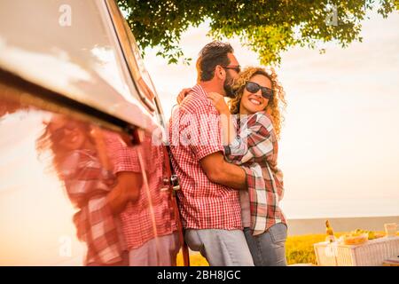 L'amour et le style de vie marié pour un couple caucasien magnifique de voyageurs embrassant et embrassant avec une camionnette rouge vintage - miroir et joyeux heureux personnes profitant de l'activité de loisirs en plein air ensemble Banque D'Images