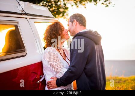 Couple l'âge moyen des profils l'homme et la femme s'embrasser avec amour au cours de plein air travel vacation - bus rouge en arrière-plan et l'heure du coucher de soleil. Banque D'Images