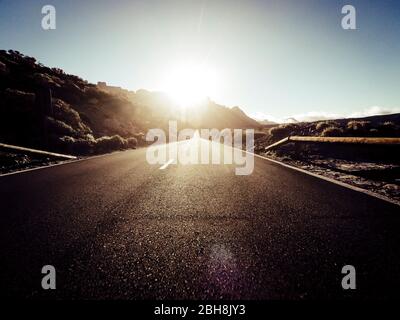 Route à long chemin à la montagne avec soleil en face et effet de lumière du soleil - point de vue du sol avec asphalte noir et lignes blanches - concept de conduite et de voyage Banque D'Images