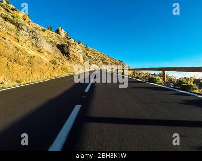 Route à long chemin à la montagne avec support vulcan devant et ciel bleu clair - point de vue au sol avec asphalte noir et lignes blanches - concept de conduite et de voyage Banque D'Images