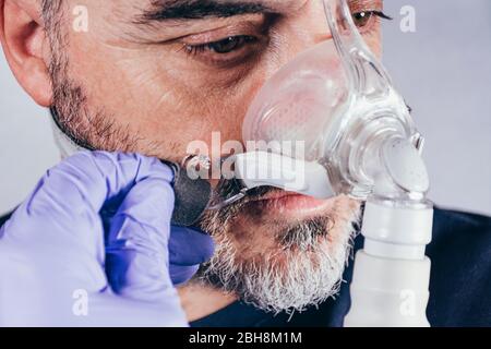 Main avec gant médical mettant sur un homme un masque respiratoire pour les troubles du sommeil. Fond blanc. Apnée. Dispositifs médicaux. Pompe à air. Apnée assistée Banque D'Images