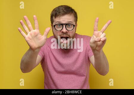 Homme joyeux et émotionnel barbu avec des lunettes, montre avec ses doigts numéro sept, sur un fond jaune. Panneau 7 Banque D'Images