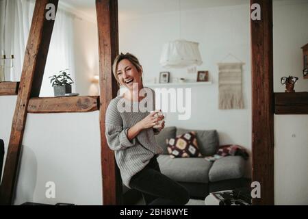junge Frau in ihrer Wohnung, hält Tasse in der Hand, lachen, Halbdéät Banque D'Images