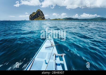 Bateau traditionnel banca arrivant incroyable île de Pinagbuyatan. Une petite île circulaire avec d'énormes falaises de calcaire et une petite plage d'Ipil avec des palmiers à noix de coco. El Nido, Palawan, Philippines. Banque D'Images
