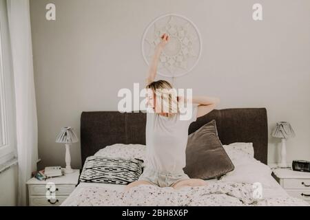 Femme assise dans un lit bâillant et s'étire Banque D'Images