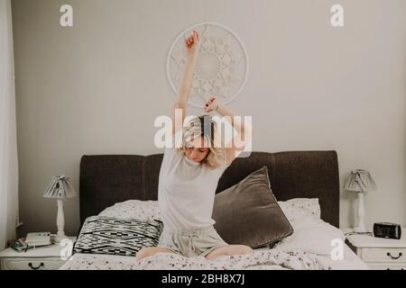 Femme assise dans le lit et s'étire Banque D'Images