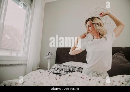 Femme assise dans le lit et s'étire Banque D'Images