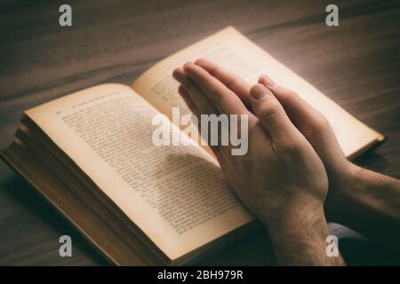 Prière, l'homme se charge d'un livre ouvert Sainte Bible, fond de bureau en bois. Concept de foi, de religion et de spiritualité Banque D'Images