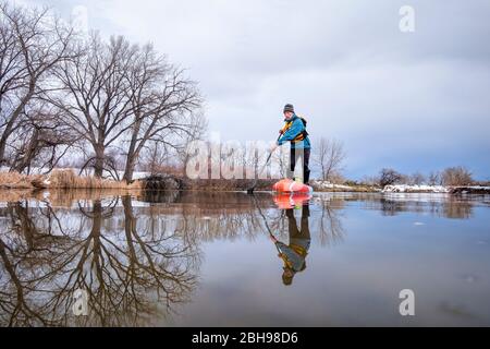 solo lac paddling comme distanciation sociale de loisirs pendant la pandémie de coronavirus, un paddler mâle senior sur stand up paddleboard au début du printemps dans Color Banque D'Images