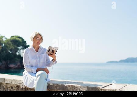 Femme souriante ayant une conversation vidéo par tablette sur fond de la mer et le ciel bleu Banque D'Images