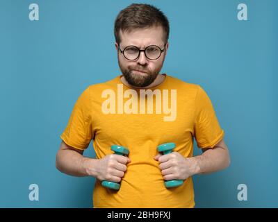 Homme barbu drôle avec surpoids a décidé d'aller pour le sport, a pris des haltères dans ses mains et est prêt pour l'entraînement. Banque D'Images