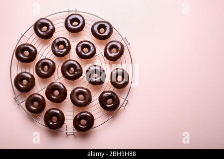 Préparation des beignets avec glaçage au chocolat sur un rack de refroidissement, sur fond rose. Couche plate de beignets chauds avec garniture de chocolat fondu. Délicieux mini-d Banque D'Images