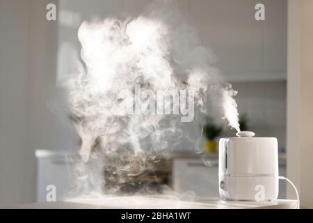 Gros plan du diffuseur d'huile aromatique sur la table à la maison, vapeur de l'humidificateur d'air. Technologie ultrasonique, augmentation de l'humidité de l'air à l'intérieur, édredon Banque D'Images