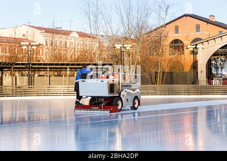 Préparation de la glace à la patinoire entre les séances de la journée ensoleillée d'hiver/ glace polie prête pour le match/ machine d'entretien de glace en mouvement, vue latérale. Banque D'Images