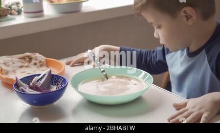 Un jeune garçon mange de la soupe assise à la table de la salle à manger Banque D'Images