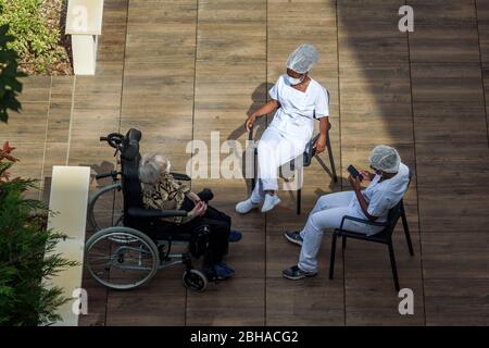 Infirmières et infirmiers s'occupant de personnes âgées dans une maison de soins pendant la pandémie de coronavirus. Les soignants qui ont une pause au soleil avec une vieille femme résidente. Banque D'Images