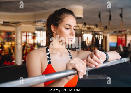 Jeune sportif séduisant debout dans la salle de gym, se reposant après des exercices, se penchant sur un rail, en vérifiant la montre de fitness Banque D'Images