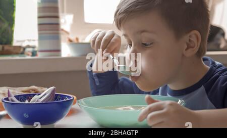 Un jeune garçon mange de la soupe assise à la table de la salle à manger Banque D'Images