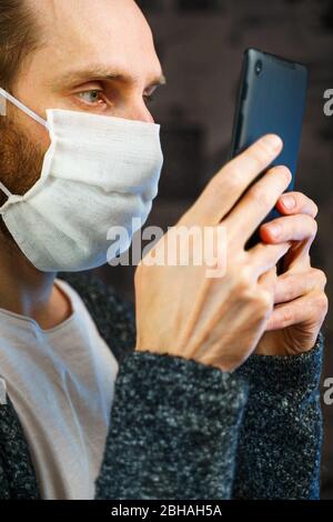 Portrait d'un homme barbu toujours en service avec un comprimé dans les mains dans un masque de gaze. Protection préventive de votre propre santé contre l'infection virale. Banque D'Images