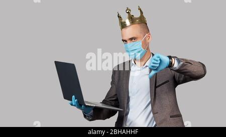 Jeune homme d'affaires dans une couronne et un masque de protection et des gants. Rester à la maison pendant la quarantaine du coronavirus Covid-19. Montre pouce vers le bas Banque D'Images