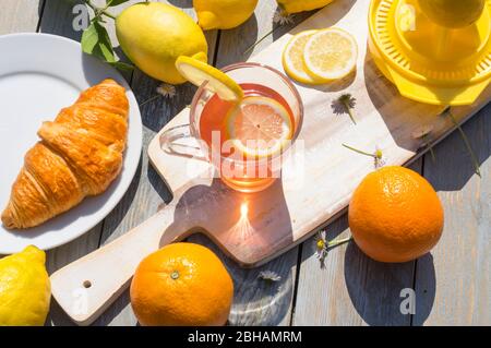 Une tasse de thé aux agrumes, petit déjeuner croissant, citrons et oranges au soleil du matin sur fond de bois Banque D'Images